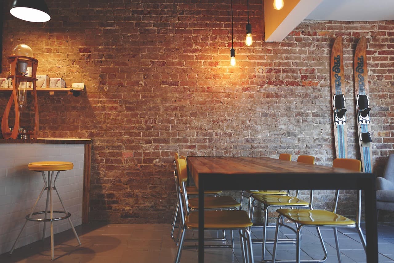 A cafe with an exposed brick wall, bar stools and wooden tables