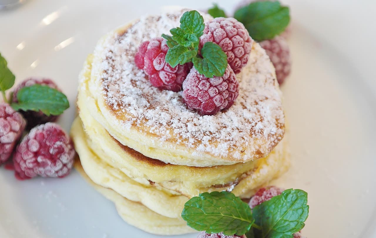 A stack of pancakes with raspberries and a dusting of icing sugar