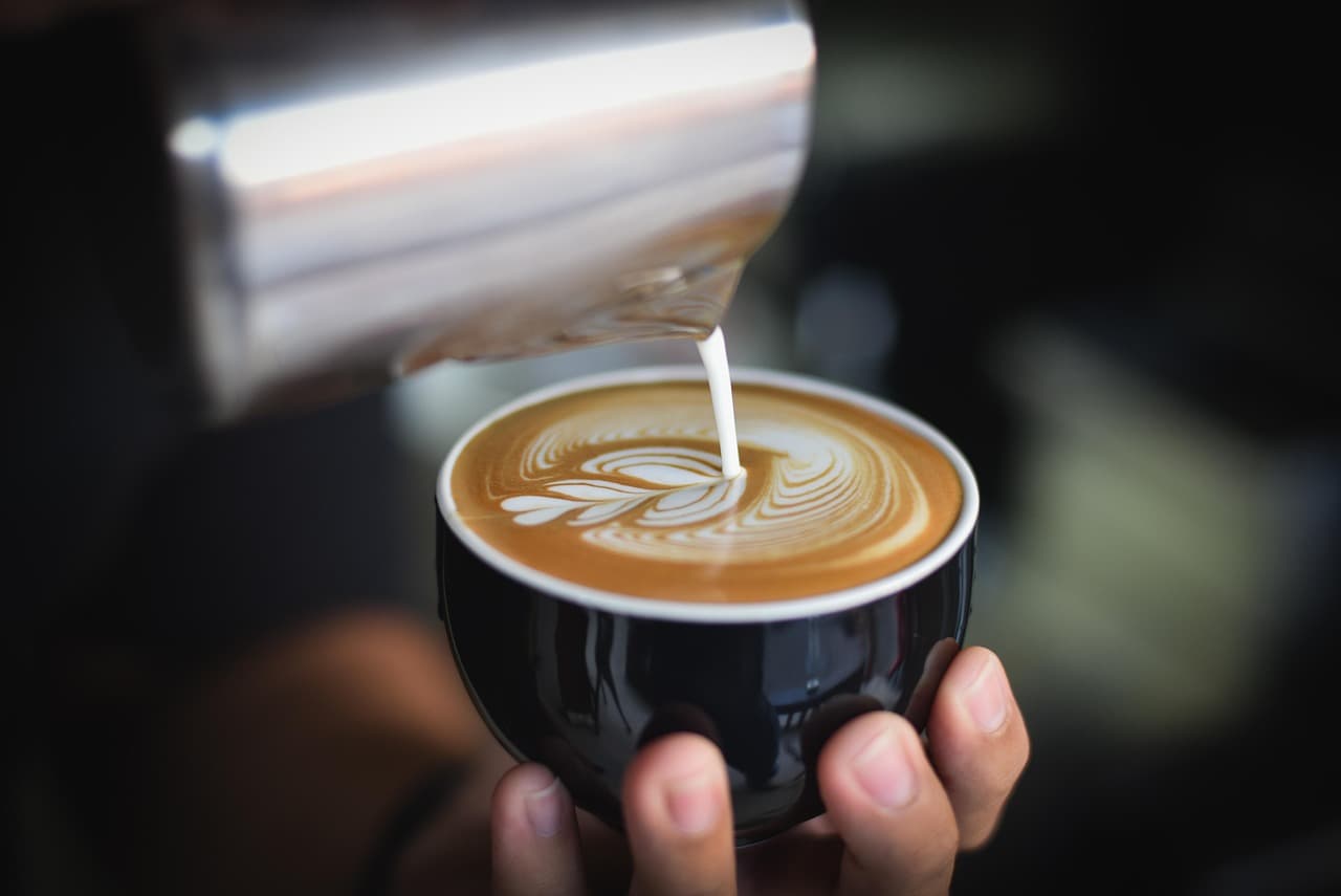A barista pouring steamed milk into a flat white