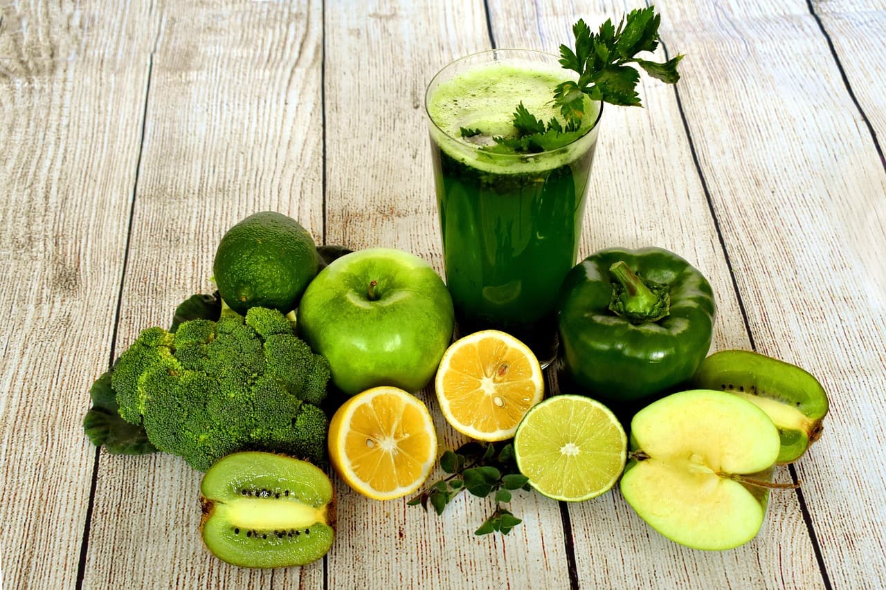 A green smoothie surrounded by fresh fruit and vegetables