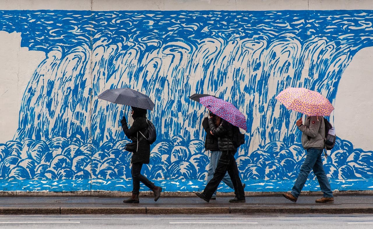 People with umbrellas walking past a blue painted mural